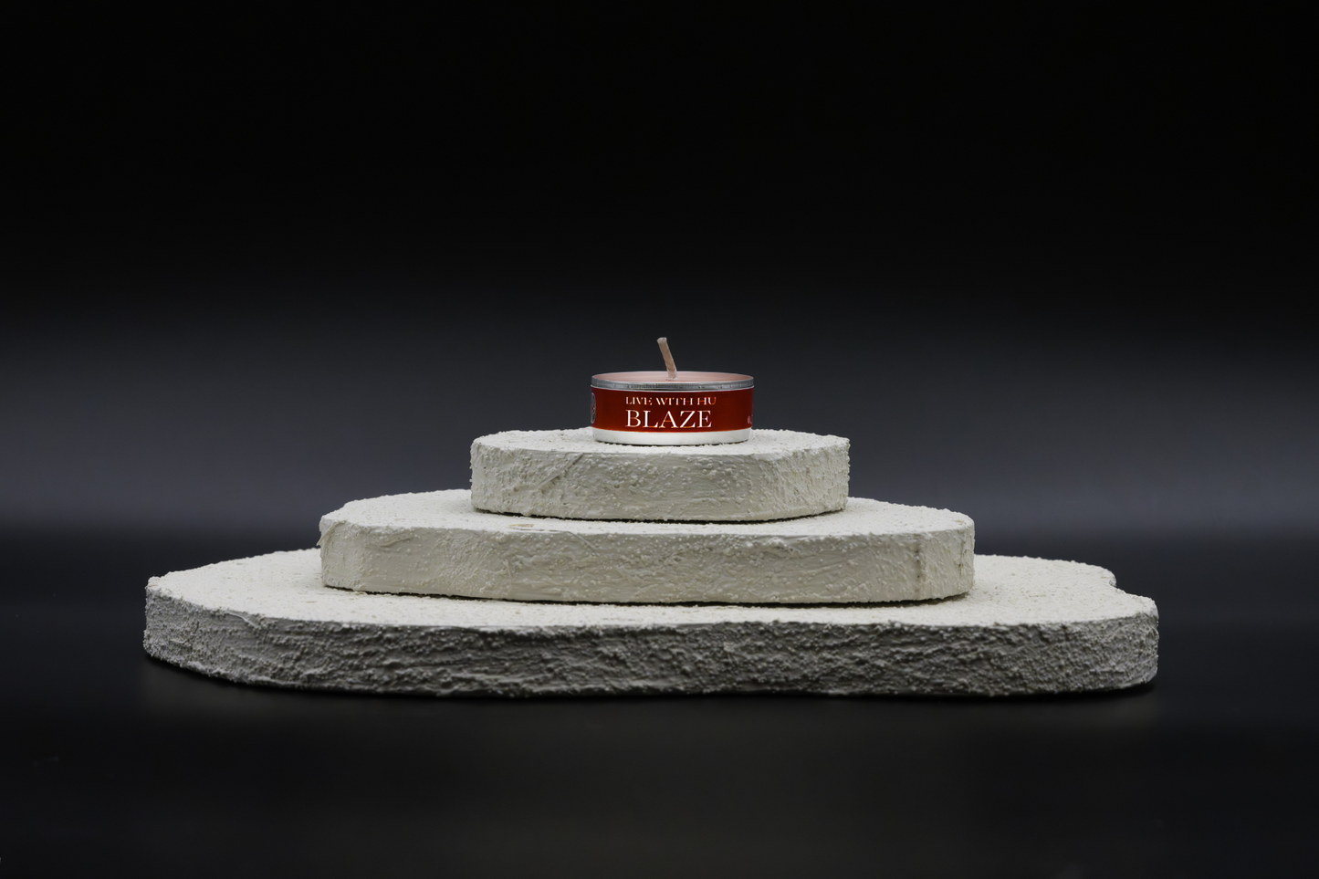 A shot of Blaze in tealights, placed on top of a three-layered white flat rocks, with black background.