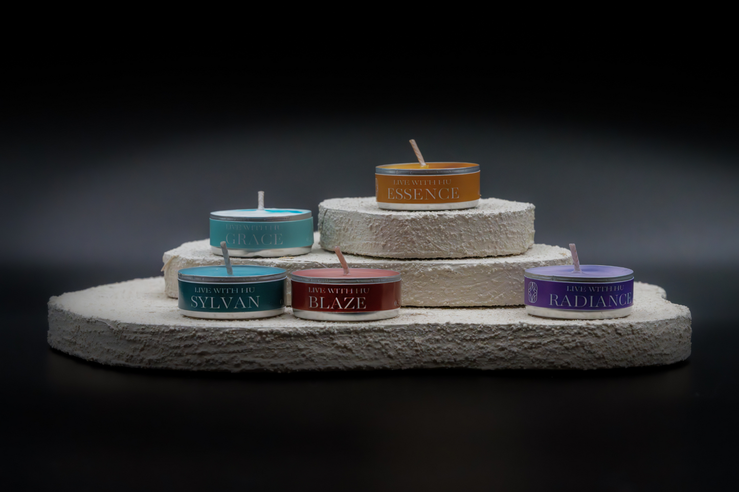 A shot of all 5 scents in tealights, placed on layered white flat rocks, with black background.