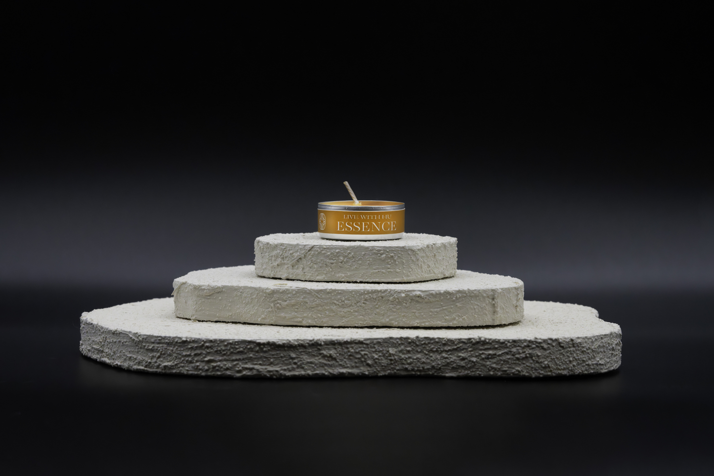 A shot of Essence in tealights, placed on top of a three-layered white flat rocks, with black background. Oriental spices inspired scent. Rich and warm