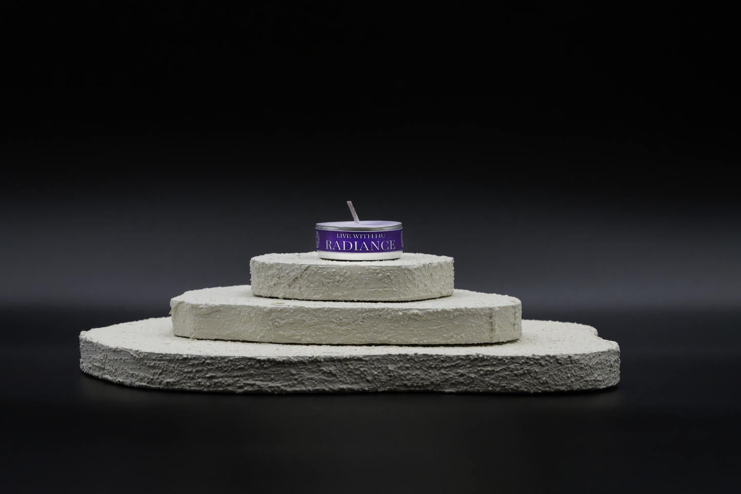 A shot of Radiance in tealights, placed on top of a three-layered white flat rocks, with black background.