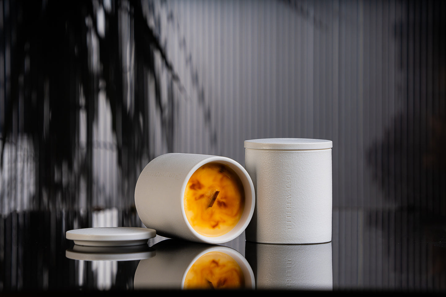 Essence candle is placed on a black reflective surface, with blurred plant shadows in the background. This portrait showcases the timeless ceramic vessel, as well as the luxury wax blend that is aesthetically colored. 