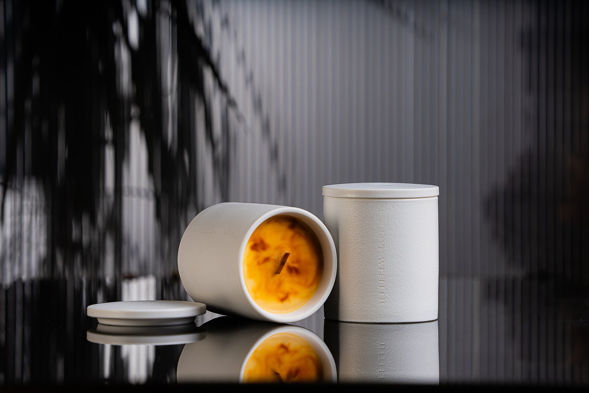 Essence candle is placed on a black reflective surface, with blurred plant shadows in the background. This portrait showcases the timeless ceramic vessel, as well as the luxury wax blend that is aesthetically colored. 