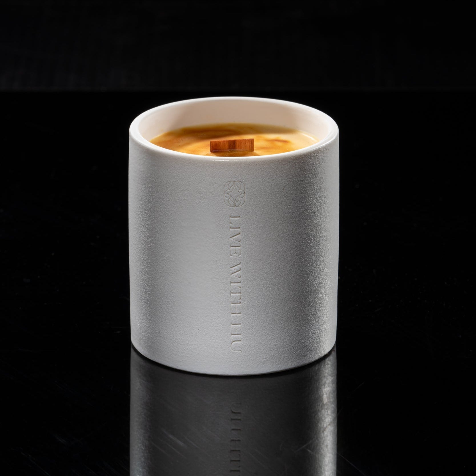 Candle in a white ceramic cup with wood wick on a black background