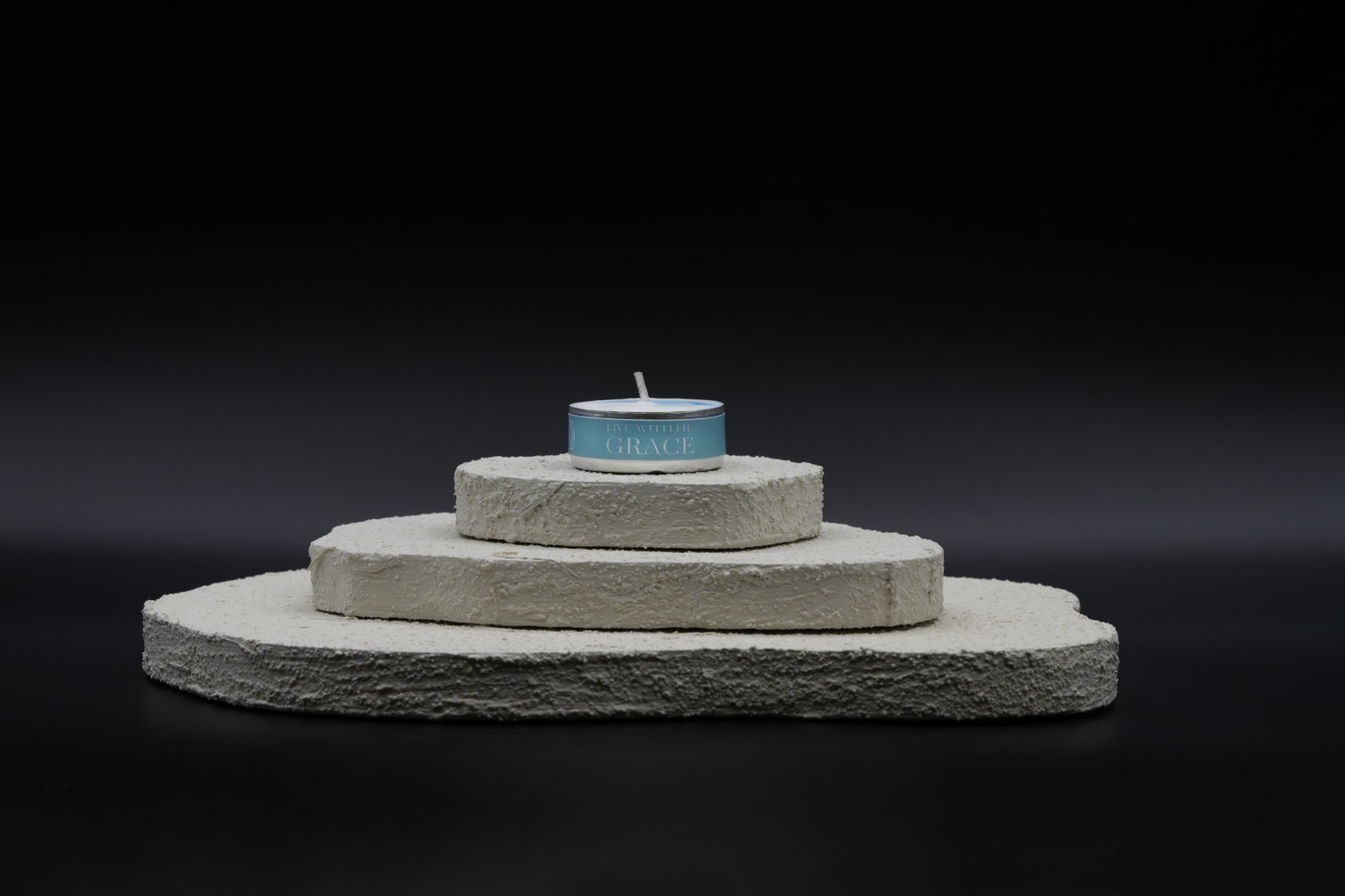 A shot of Grace in tealights, placed on top of a three-layered white flat rocks, with black background.